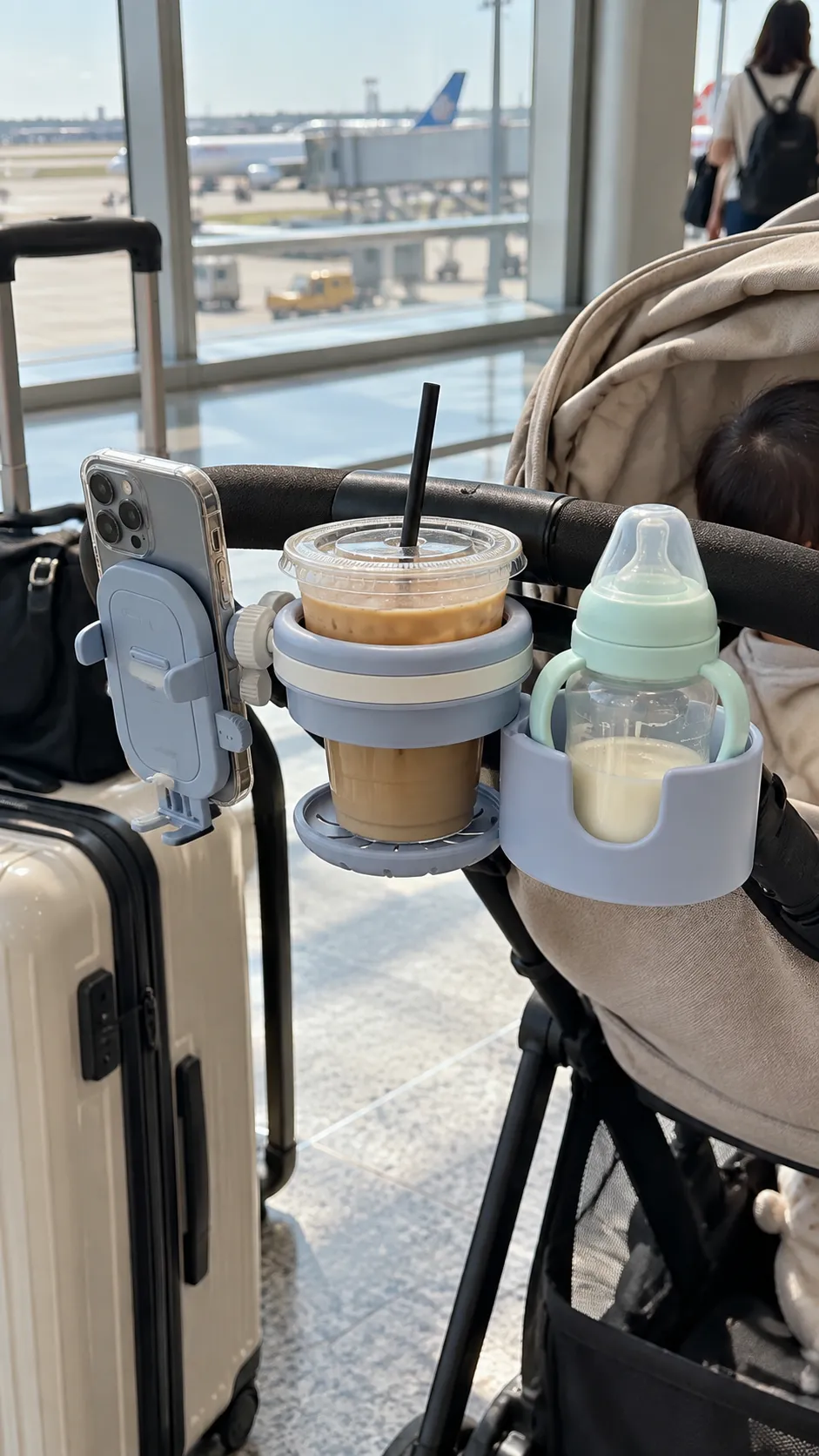 Stroller cup holder with an iced coffee, a baby bottle, and a phone